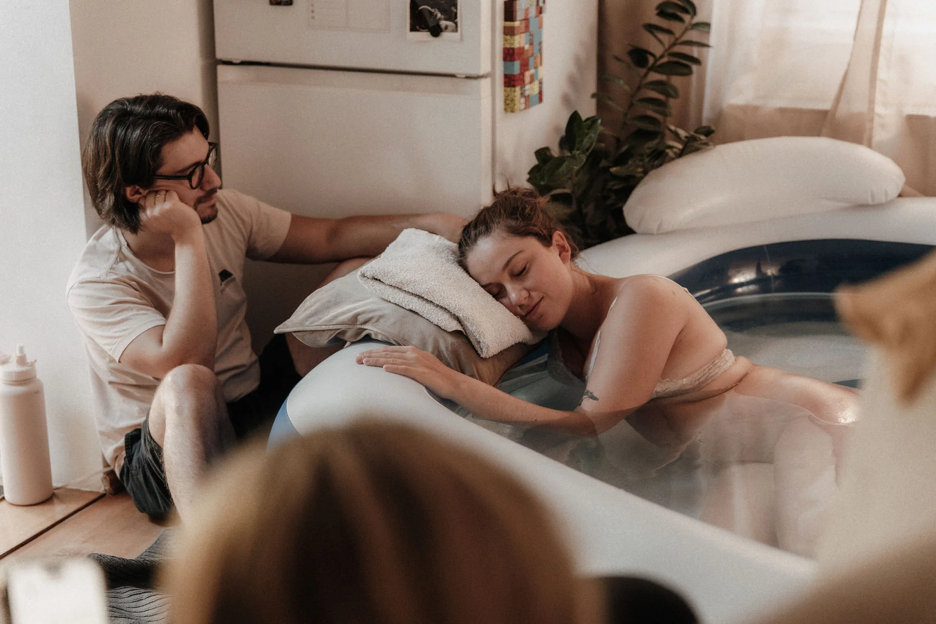 Eine Frau ruht am Geburtspool, ihr Partner sitzt neben ihr