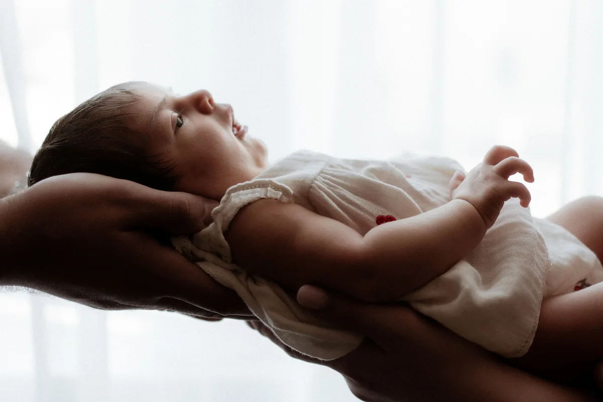 Ein Baby liegt im Studio geborgen in den Händen eines Elternteils am Fenster